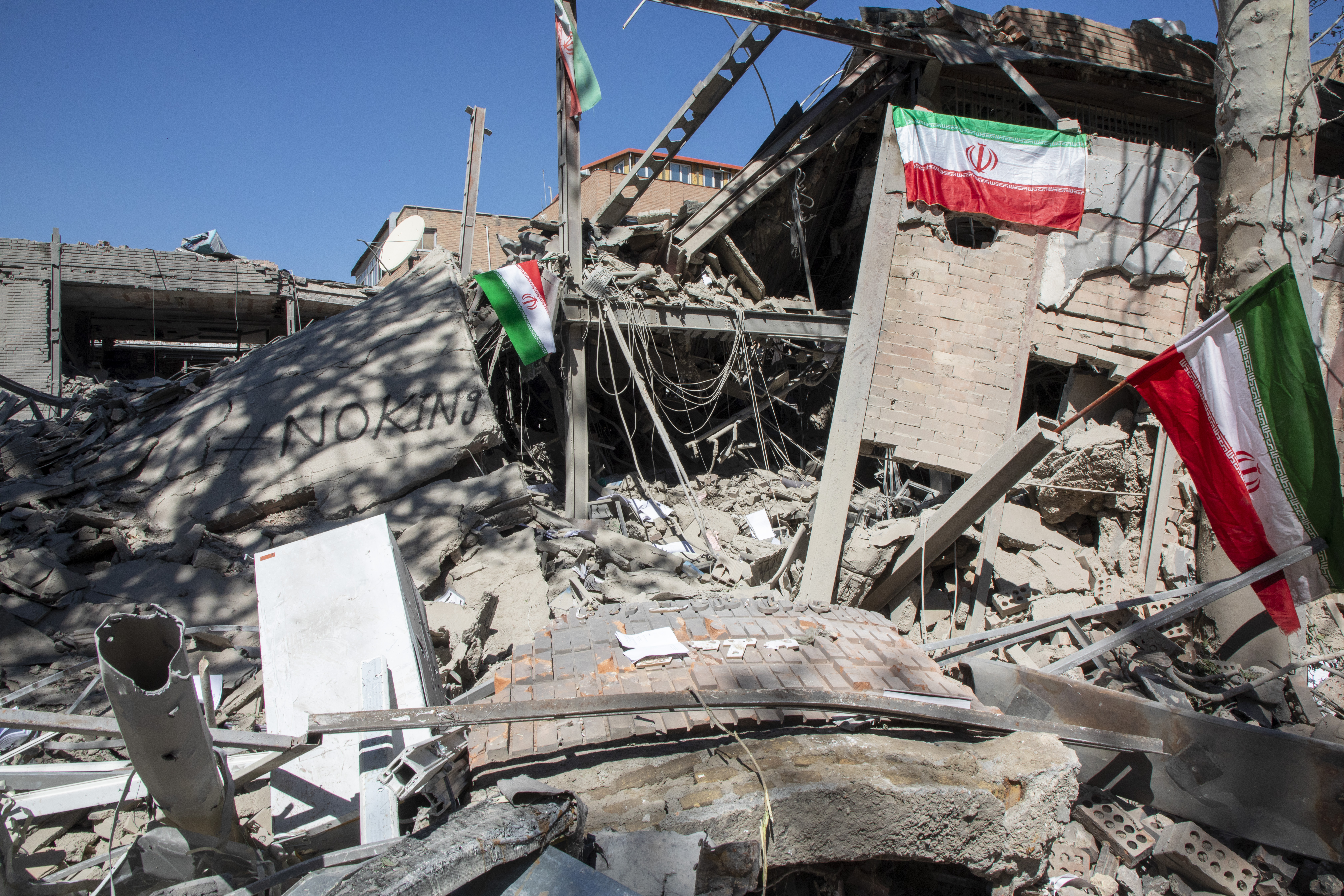 Iranian flags and graffiti reading 'No King' are seen amongst debris.