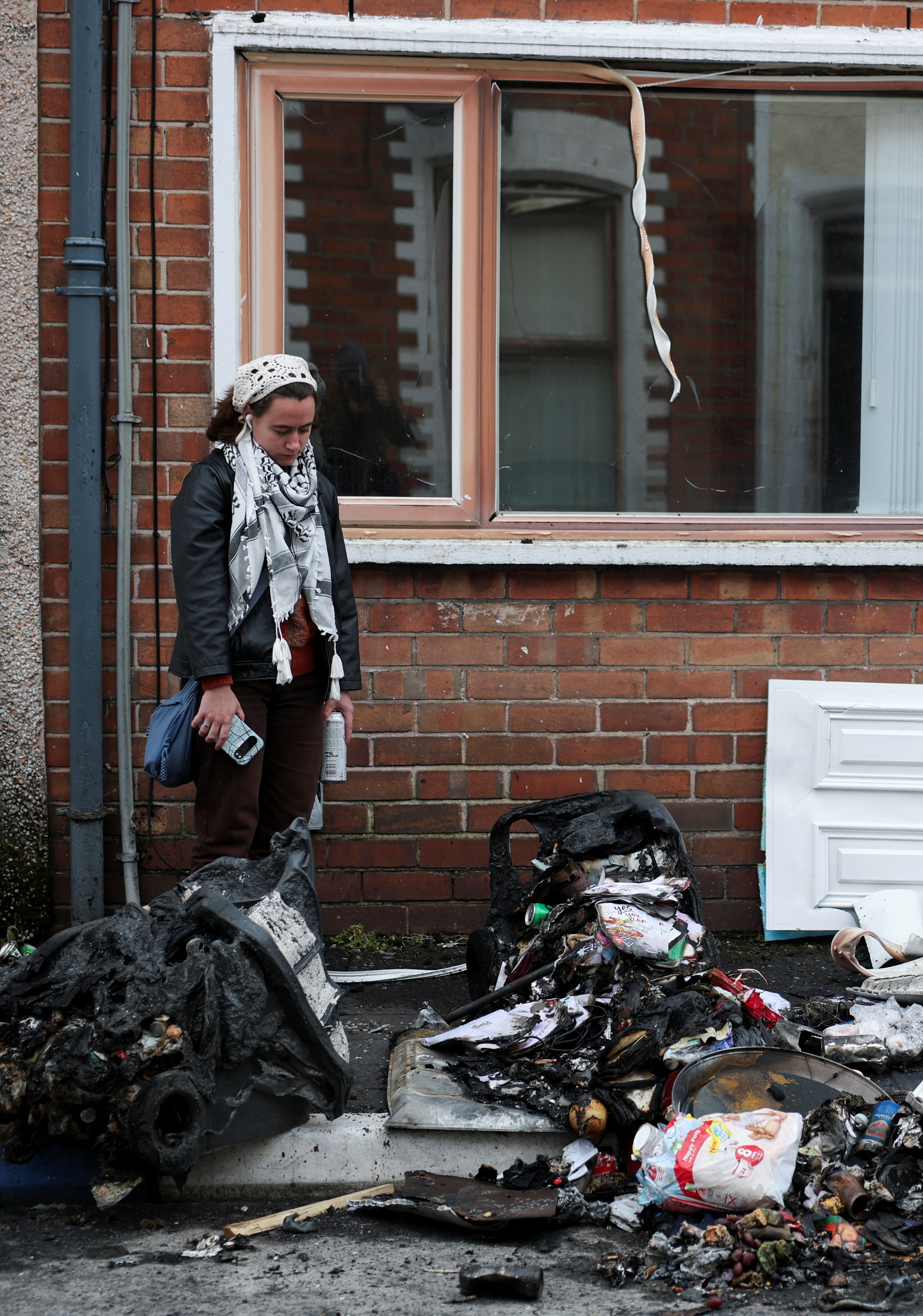 A resident looks at the charred debris scattered on the street in her neighbourhood, in the aftermath of anti-immigrant protests following a knife attack on June 8, which left a man seriously injured and prompted police to declare a critical incident, at Lendrick street, east Belfast, Northern Ireland, June 10, 2026. REUTERS/Isabel Infantes