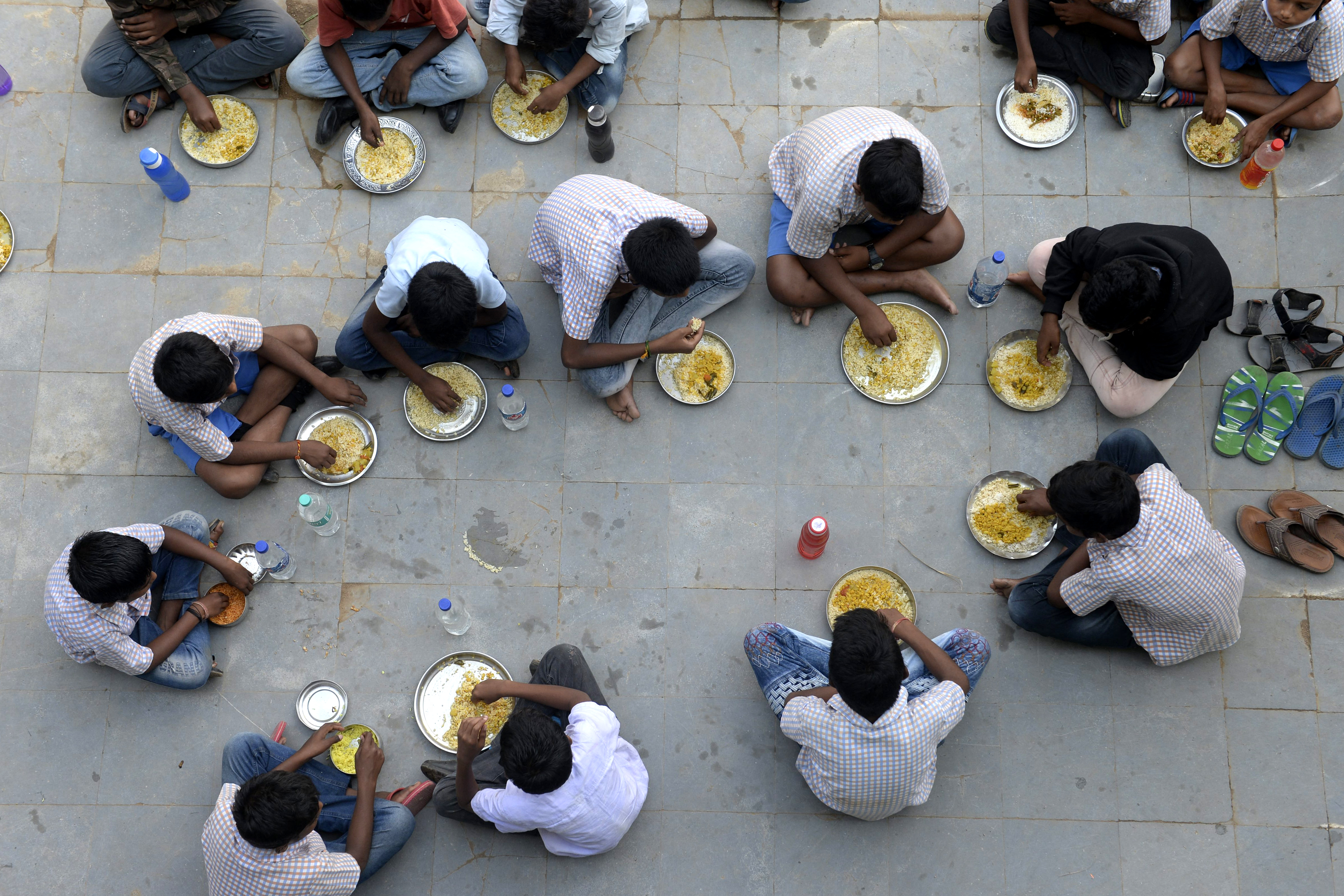 Students eat their mid-day meal during lunch break at a government high school on the outskirts of Hyderabad on November 23, 2021, as schools reopen after months due to the Covid-19 coronavirus pandemic. (Photo by NOAH SEELAM / AFP)