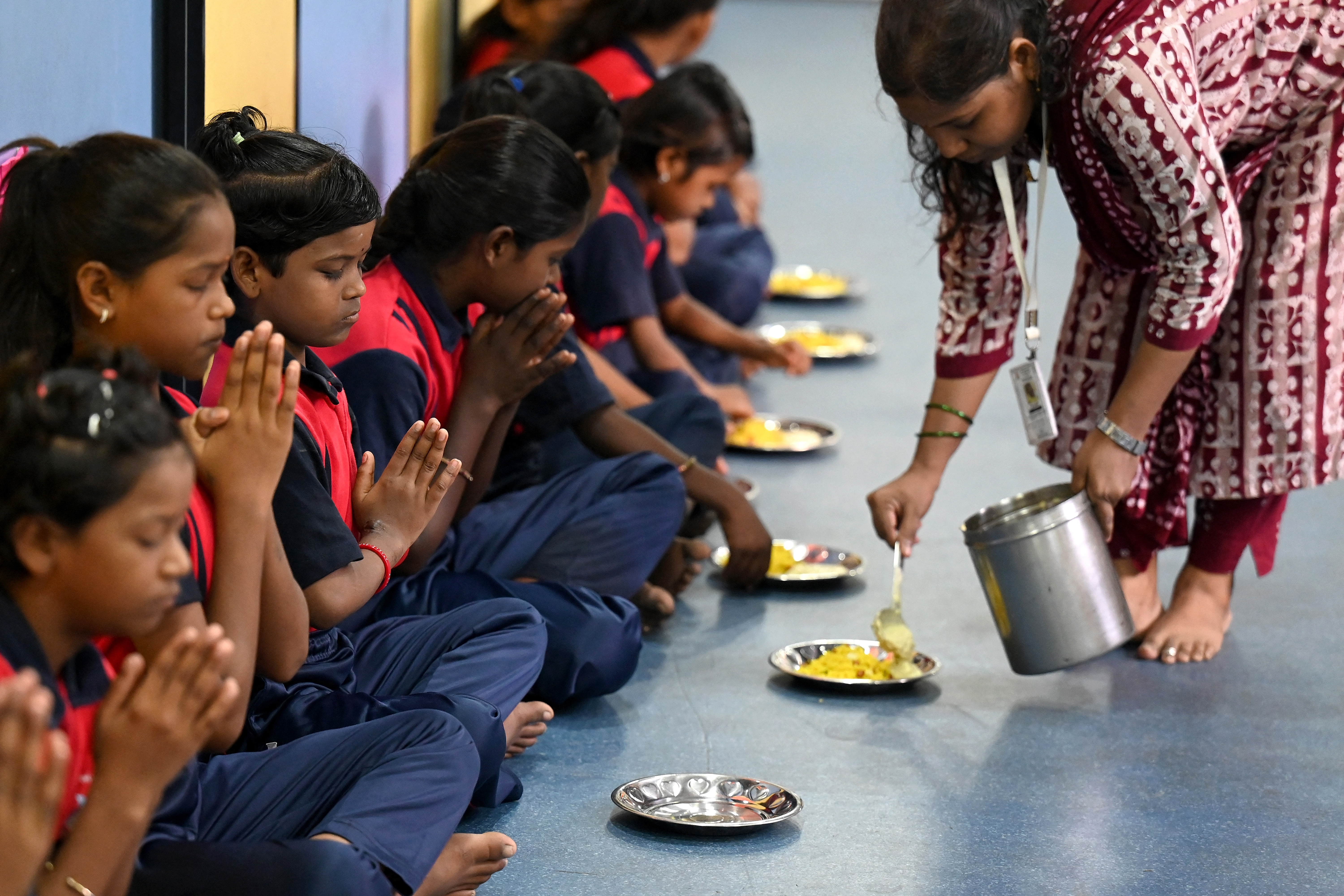 This photograph taken on May 18, 2026 shows children offering prayers before breakfast at the "Signal Shala", or traffic signal school, under a bridge in Mumbai. Beneath a busy flyover in India's financial capital Mumbai, a row of pastel-coloured shipping containers houses an unlikely school serving some of the city's most marginalised children. (Photo by Punit PARANJPE / AFP)