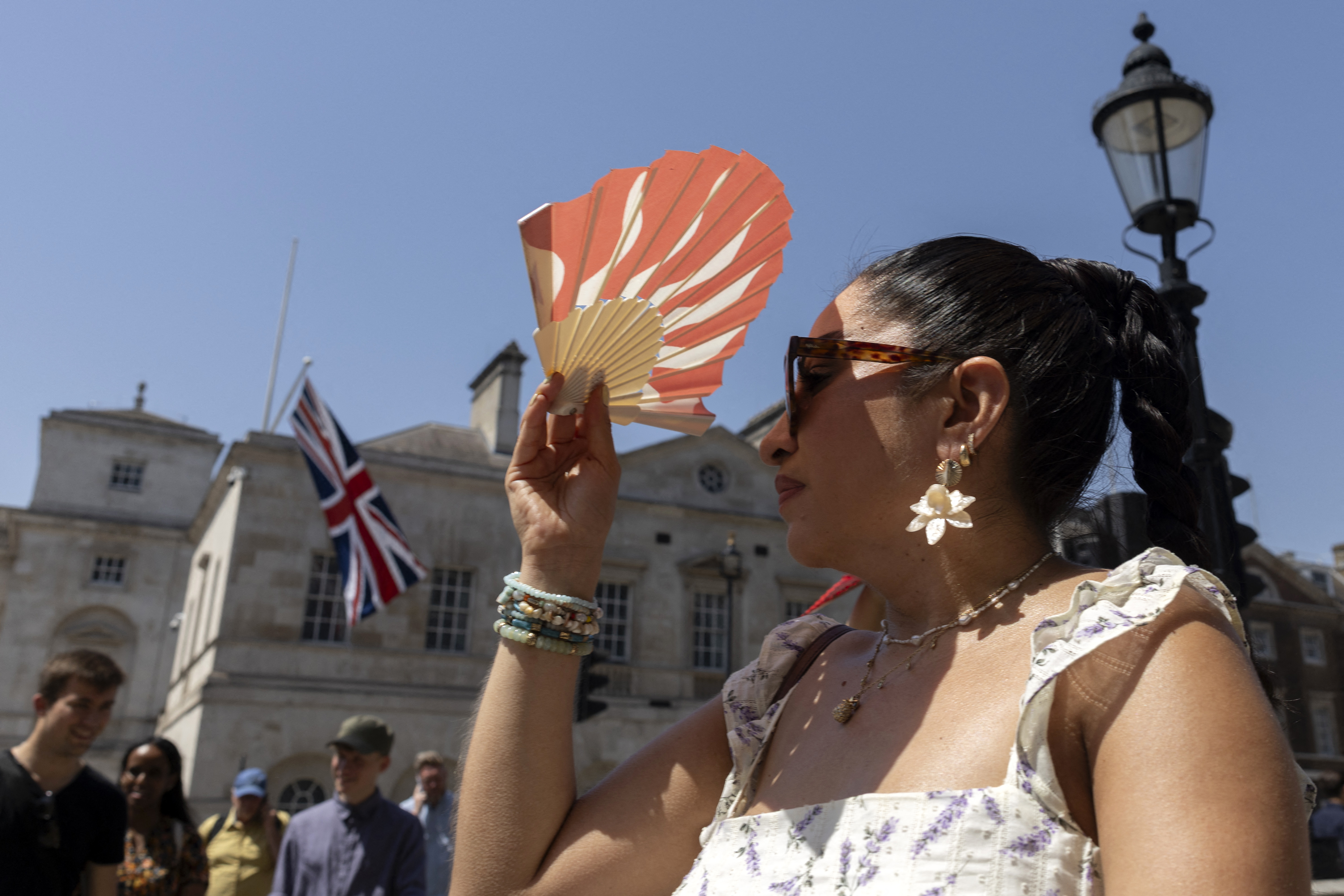 A person shields their face from the heat of the sun with a fan, in central London on June 25, 2026,