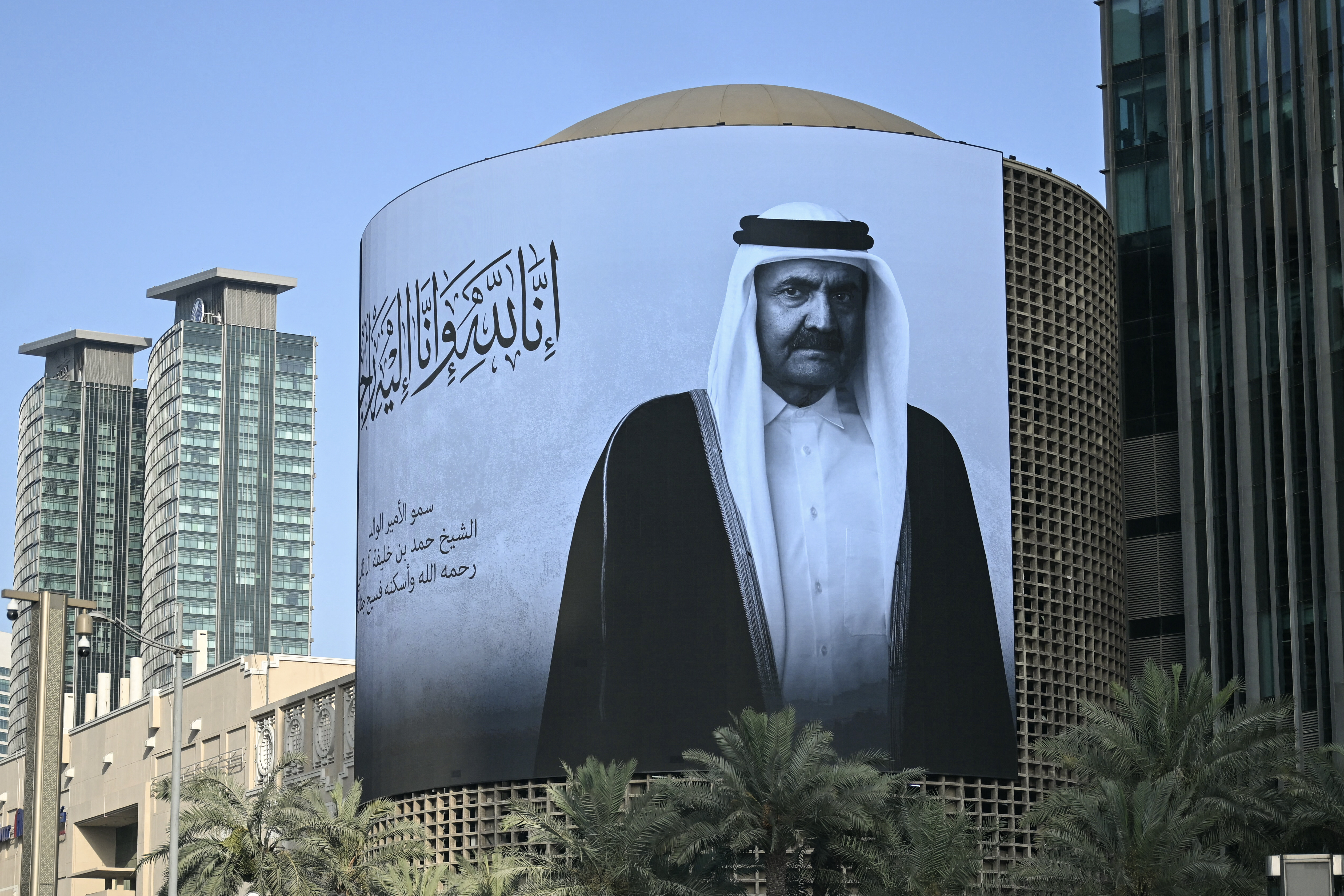 A photograph shows a billboard bearing a portrait of Qatar's former leader Sheikh Hamad bin Khalifa Al Thani in Doha on July 12, 2026, after the announcement of his death. The former leader was seen as one of the key architects of modern Qatar and led the country during a period of rapid economic growth. He took power in June 1995, overthrowing his father in a bloodless coup while the latter was abroad. In June 2013, he surprised many by voluntarily abdicating in favour of his son, Sheikh Tamim, a first in the recent history of the Arab world. (Photo by Mahmud HAMS / AFP)