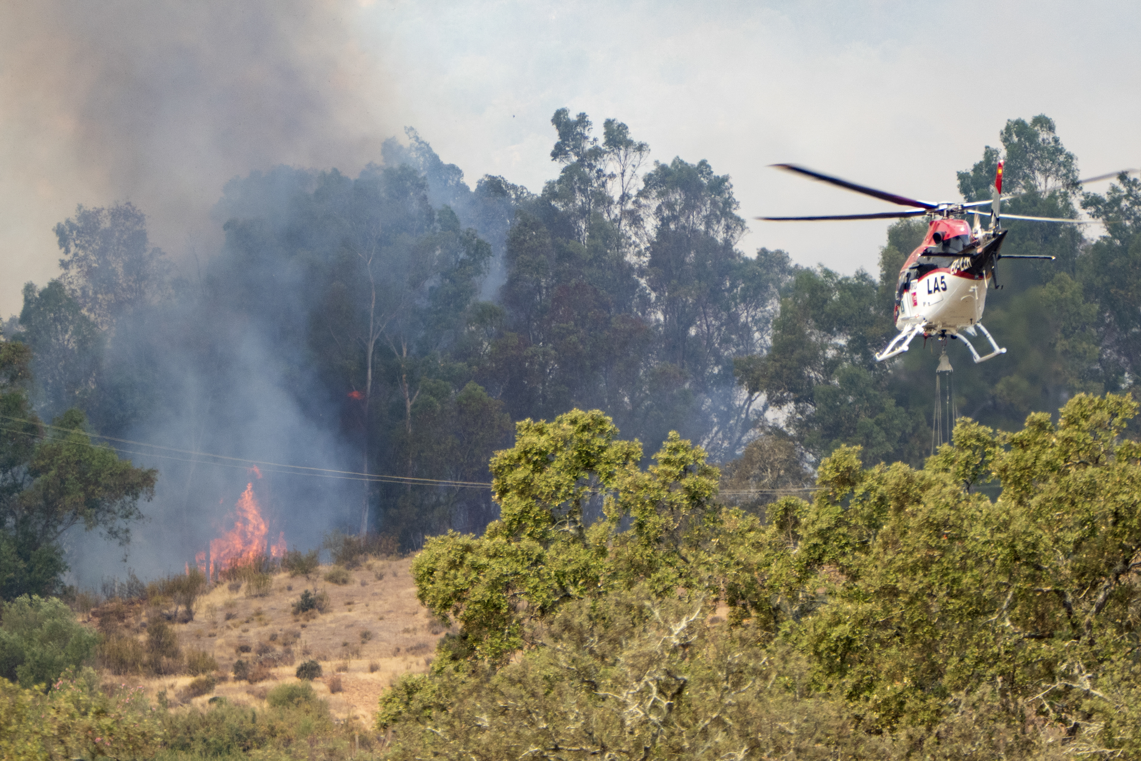 epa13126375 A fire-fighting helicopter works to extinguish a fire that broke out late 21 July at El Cerro del Andevalo (Huelva), Spain, 22 July 2026. The fire affects an area of pastureland with a dense population of eucalyptus trees, holm oaks and scrub, which is helping the flames to spread and making it difficult to extinguish the fire. EPA/DAVID ARJONA