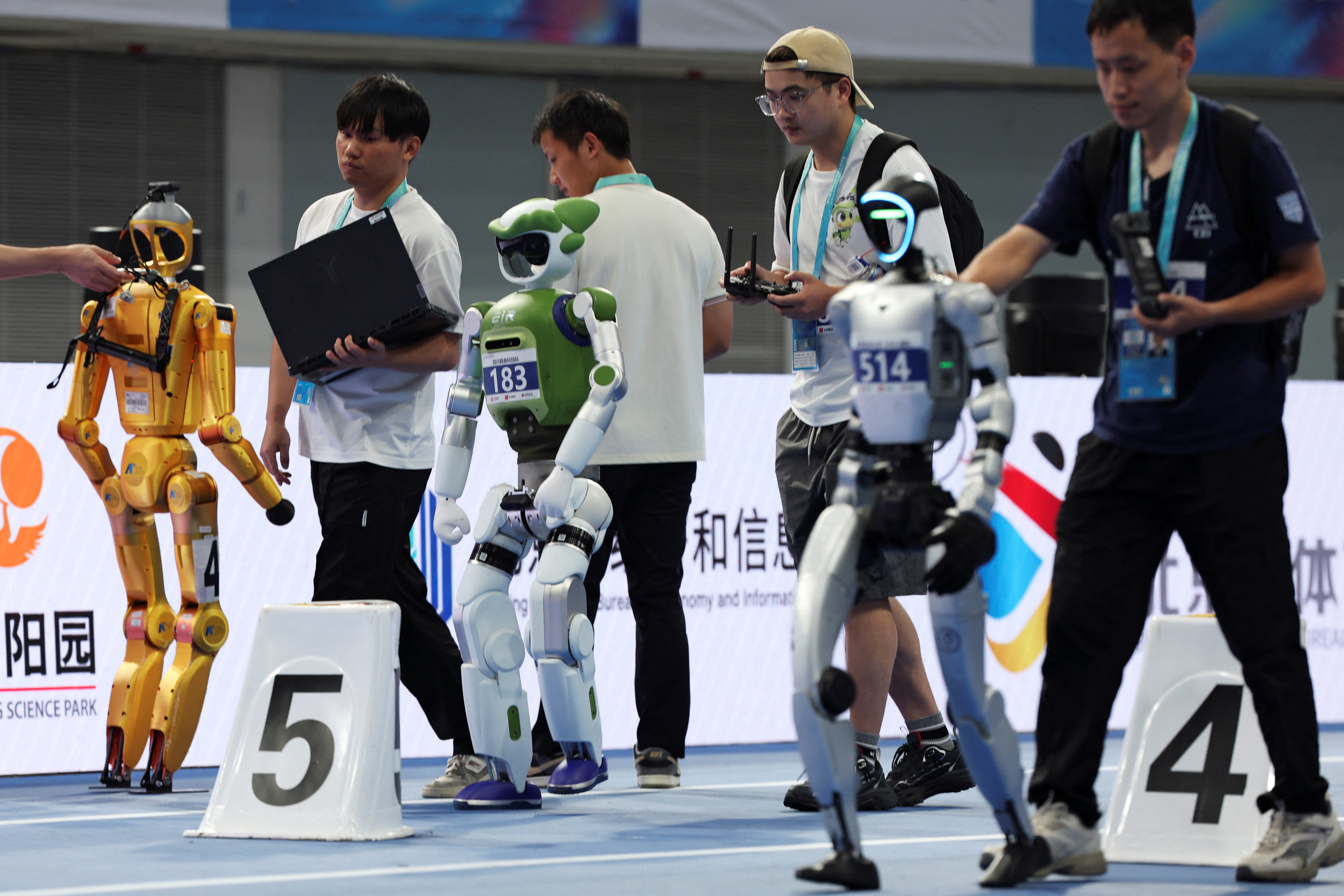 Participants help humanoid robots get in position at the starting line before a 100m small-size group race, during the second World Humanoid Robot Games at the National Speed Skating Oval in Beijing, China