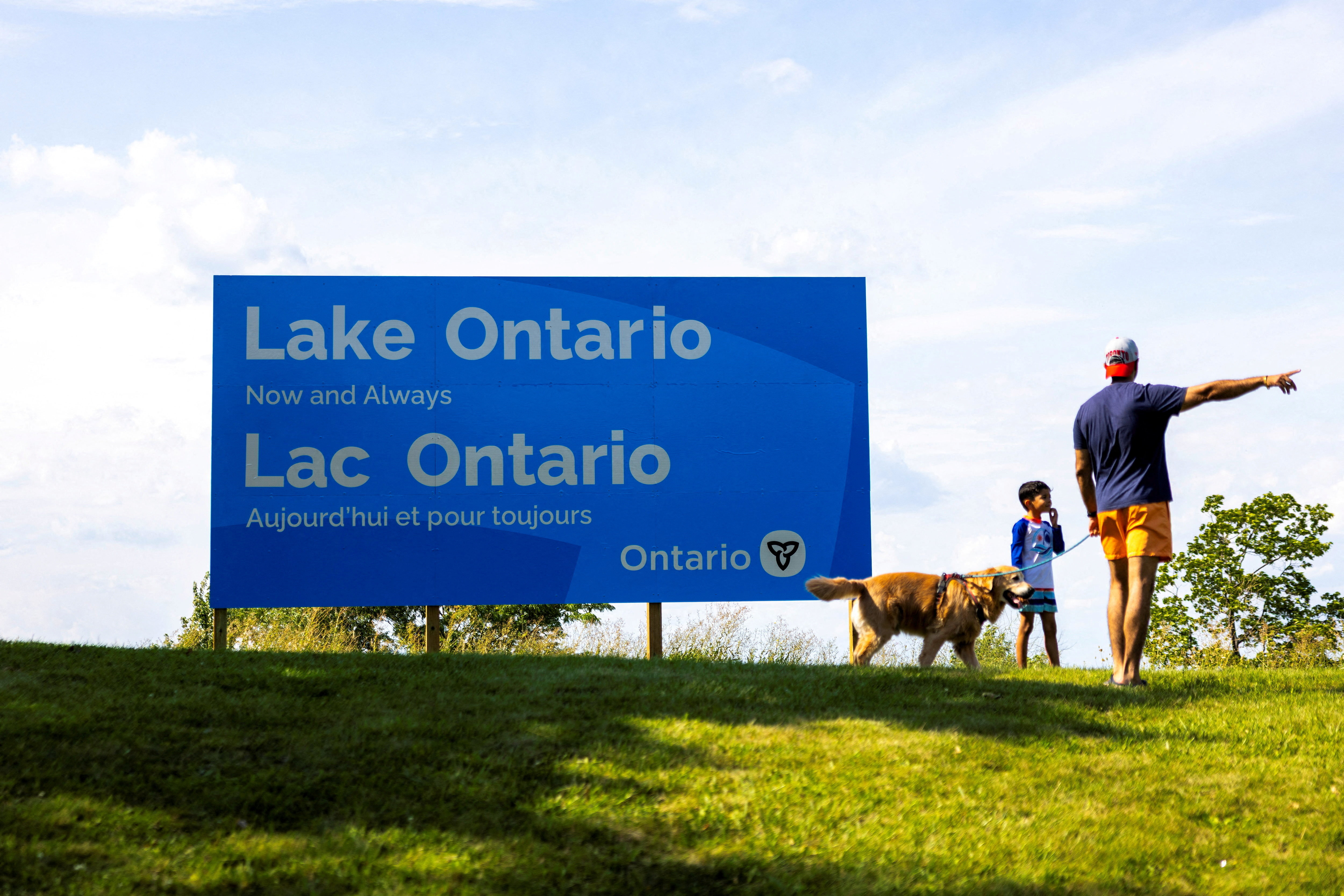 A family walks past a sign reading ‘Lake Ontario, Now and Always’, near Grimsby, Ontario, Canada, on August 29, 2026, after Trump ordered the lake renamed ‘Lake America’