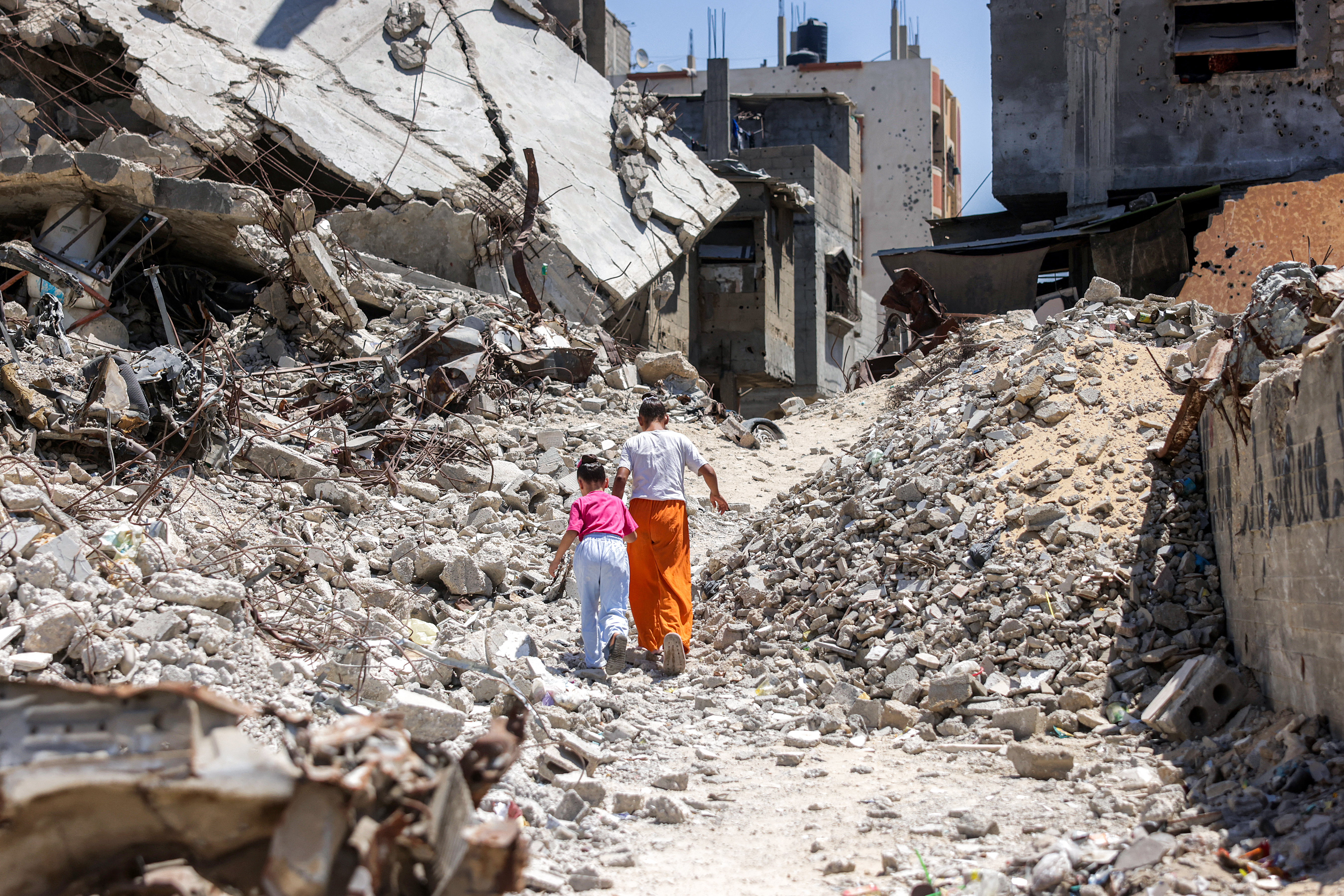 Two girls walk past the rubble of collapsed buildings in Khan Yunis in the southern Gaza Strip on August 25, 2026.