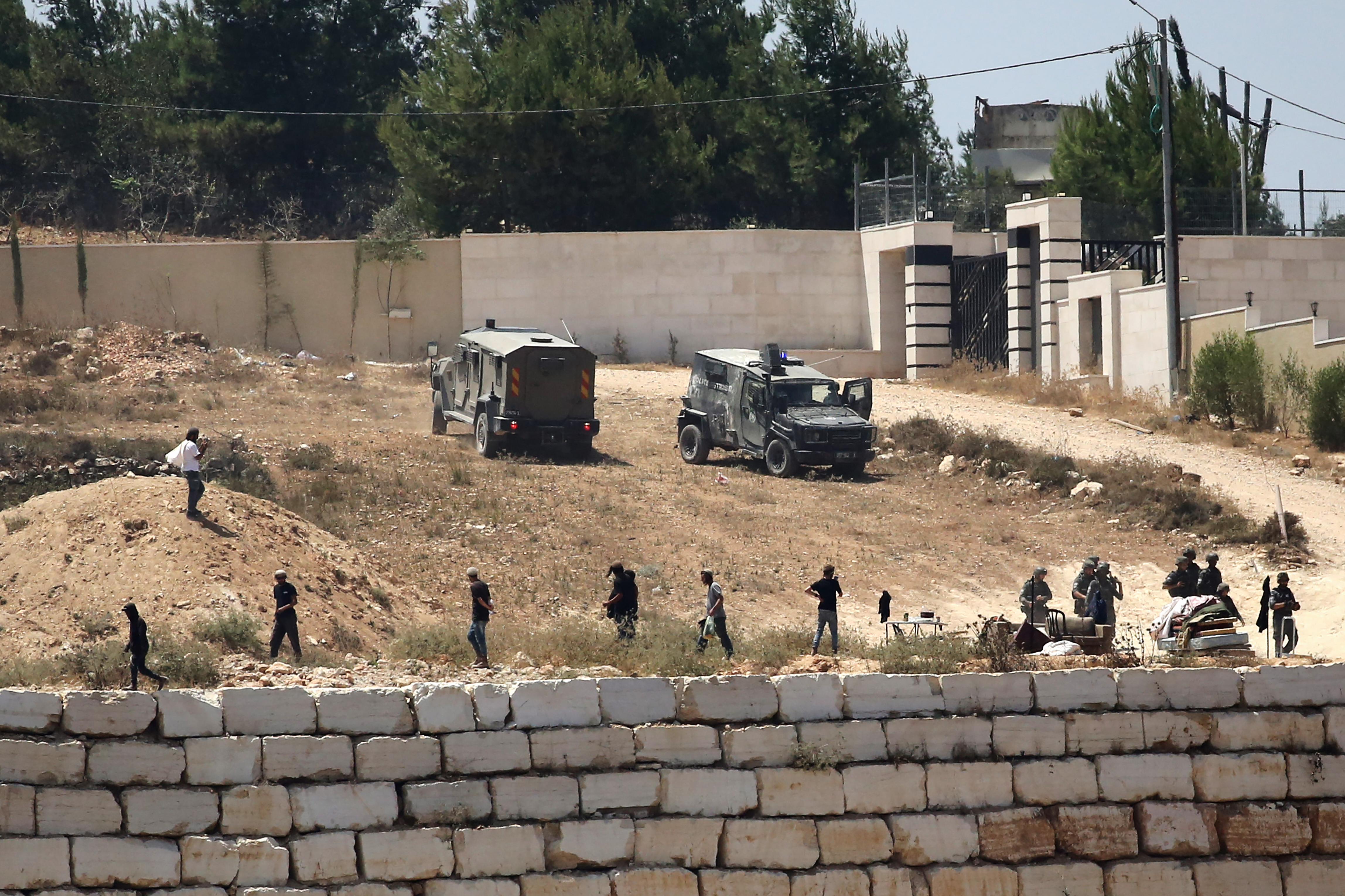 Israeli soldiers stand guard next to settlers in front of Palestinian homes that they have blockaded in the village of Qusra, south of Nablus, in the occupied West Bank, Wednesday, Aug. 12, 2026. (AP Photo/Nidal Eshtayeh)