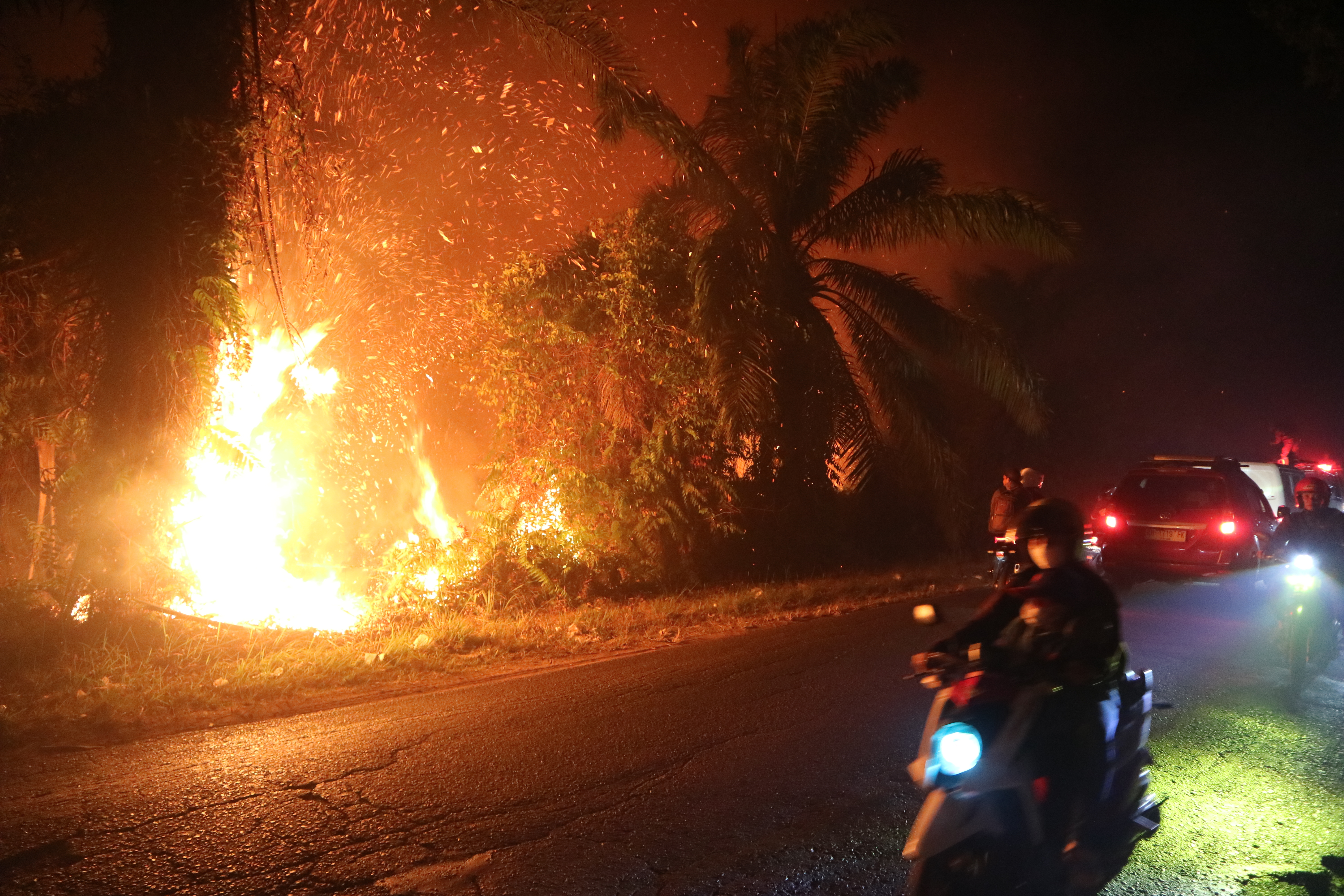 Motorists ride past a wildfire burning through a peatland field in Sampit, Central Kalimantan, Indonesia, on August 24, 2026
