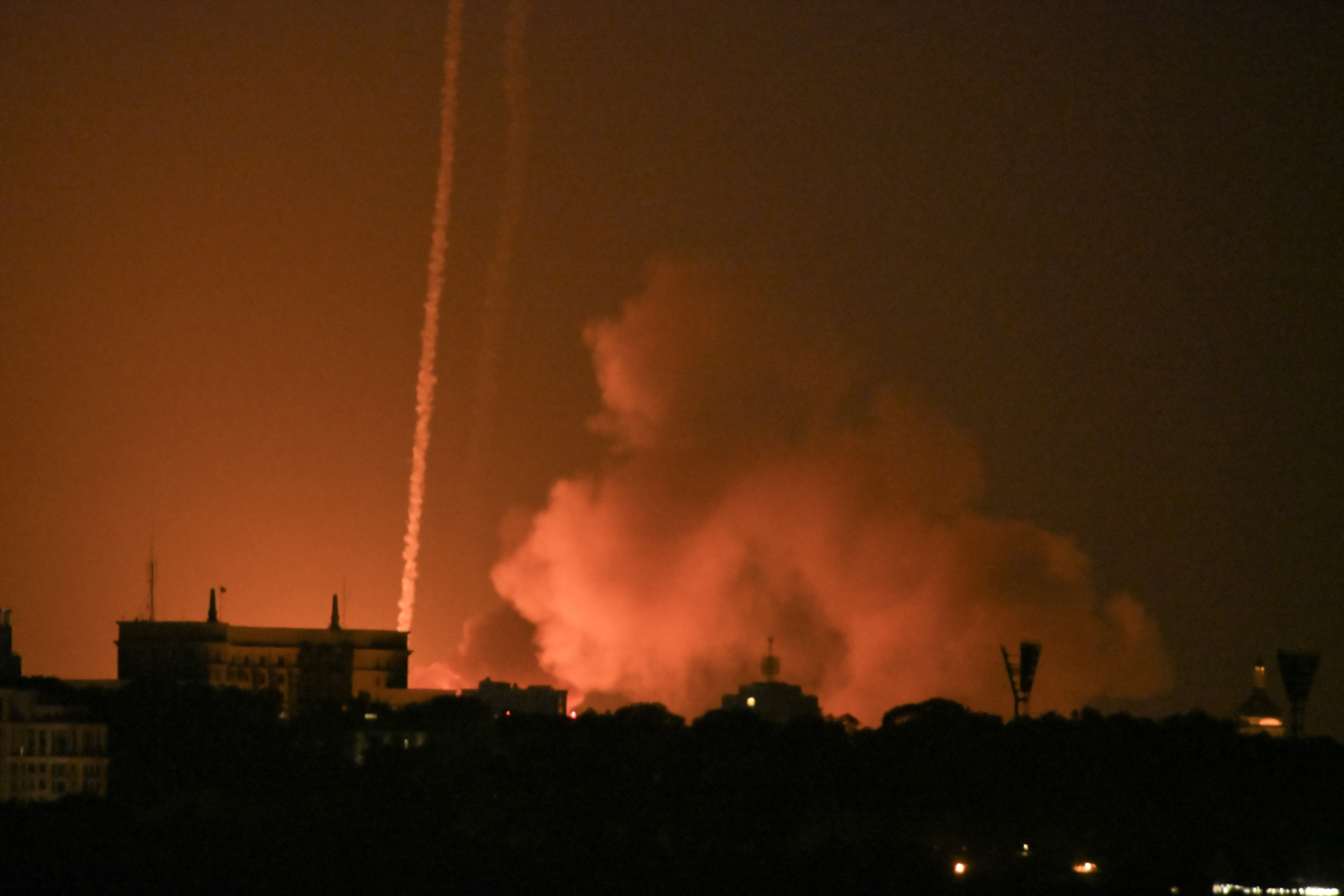 Smoke rises above buildings at night.