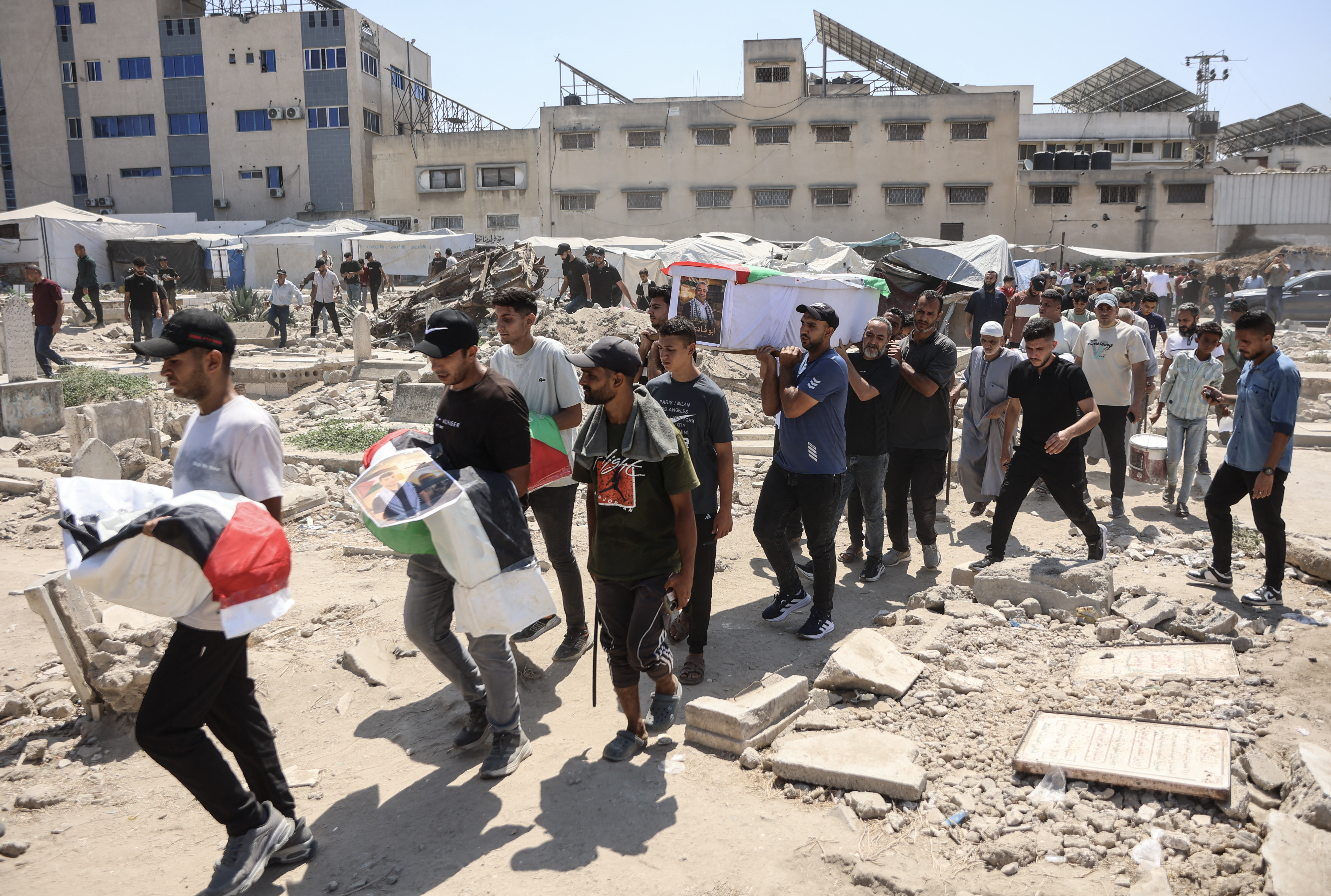 Mourners carry flag-draped body bags containing the remains of Palestinians killed in Israeli strikes during the war with Hamas and recently recovered from the rubble, during a mass funeral in Gaza City on August 20, 2026.
