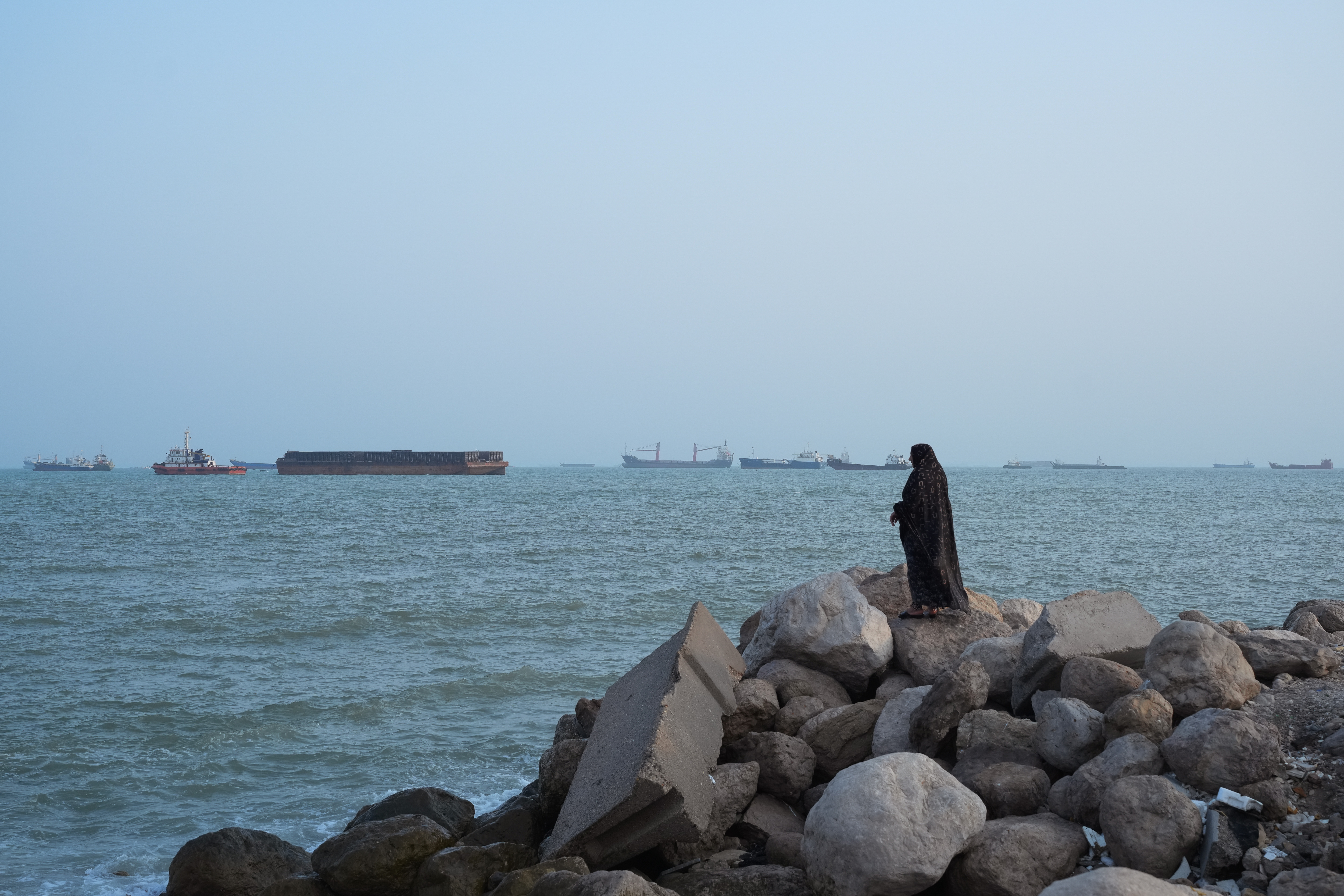 BANDAR ABBAS, IRAN - AUGUST 10: A women stands overlooking the water as ships are seen anchored in the Strait of Hormuz on August 10, 2026 off the coast of Bandar Abbas, Iran. In a recent statement, Iran's Supreme National Security Council said the vital waterway would not reopen until the United States corrects its behavior, demanding that the U.S. end its war on Iran and compensate the country for war damage, among other conditions. Iran has largely halted vessel traffic through the strait with the threat of strikes; meanwhile, the U.S. has imposed a blockade on Iranian ports. (Photo by Ali Saeedi/Getty Images)