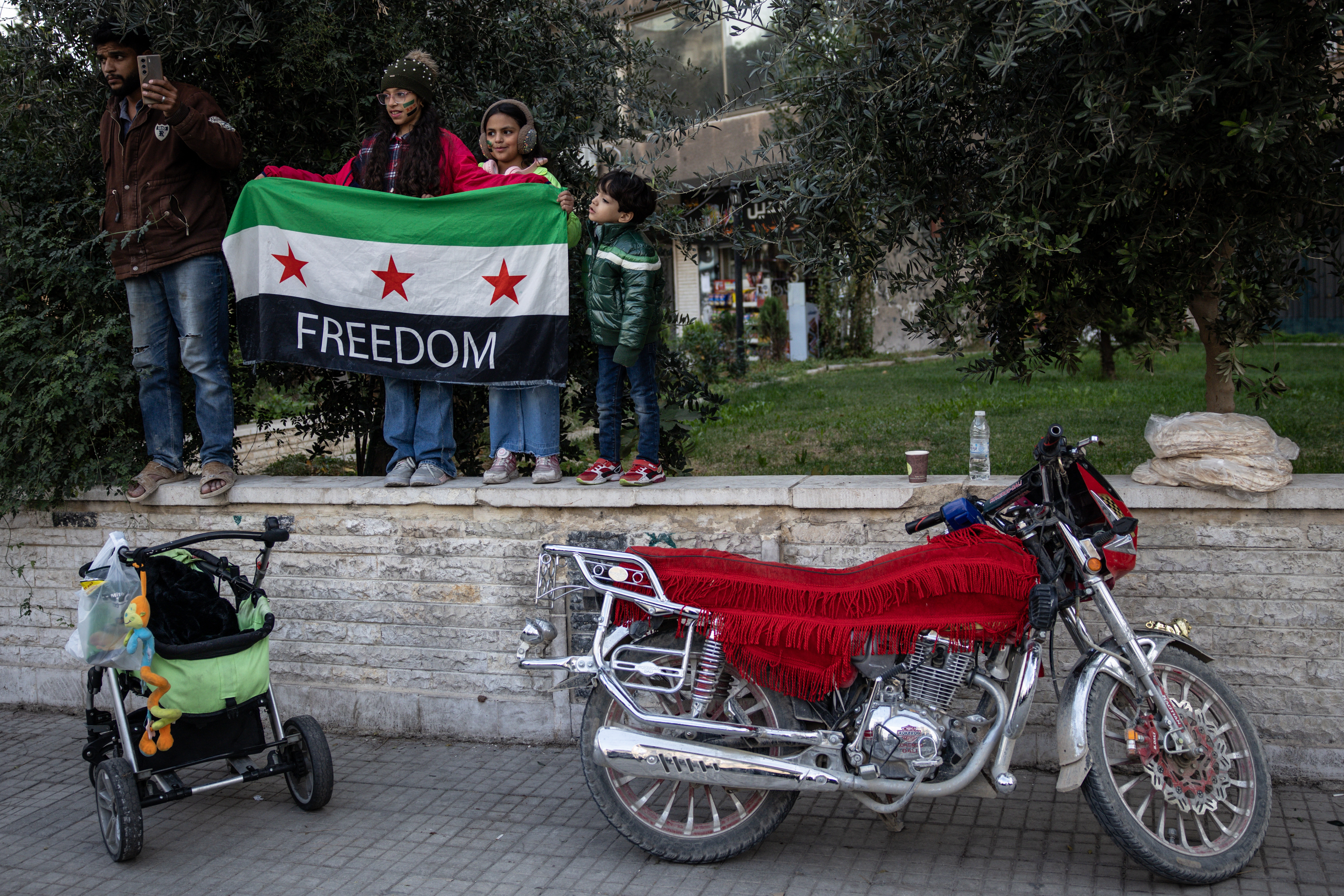 DAMASCUS, SYRIA - DECEMBER 08: People watch soldiers and military vehicles parade through the streets to mark one year since the fall of the Assad regime on December 8, 2025 in Damascus, Syria. The first anniversary of the fall of the Assad regime in Syria is being marked today across the country. Former leader Bashar al-Assad was granted asylum in Russia after he fled the country and his government collapsed on December 8, 2024. The fall of the regime, which ended over five decades of the Assad family's rule, came after a rapid offensive by opposition forces led by Hayat Tahrir al-Sham (HTS). A transitional government, headed by Ahmed al-Sharaa (formerly the HTS leader), is now in place and working on the country's reconstruction and political transition. (Photo by Chris McGrath/Getty Images)