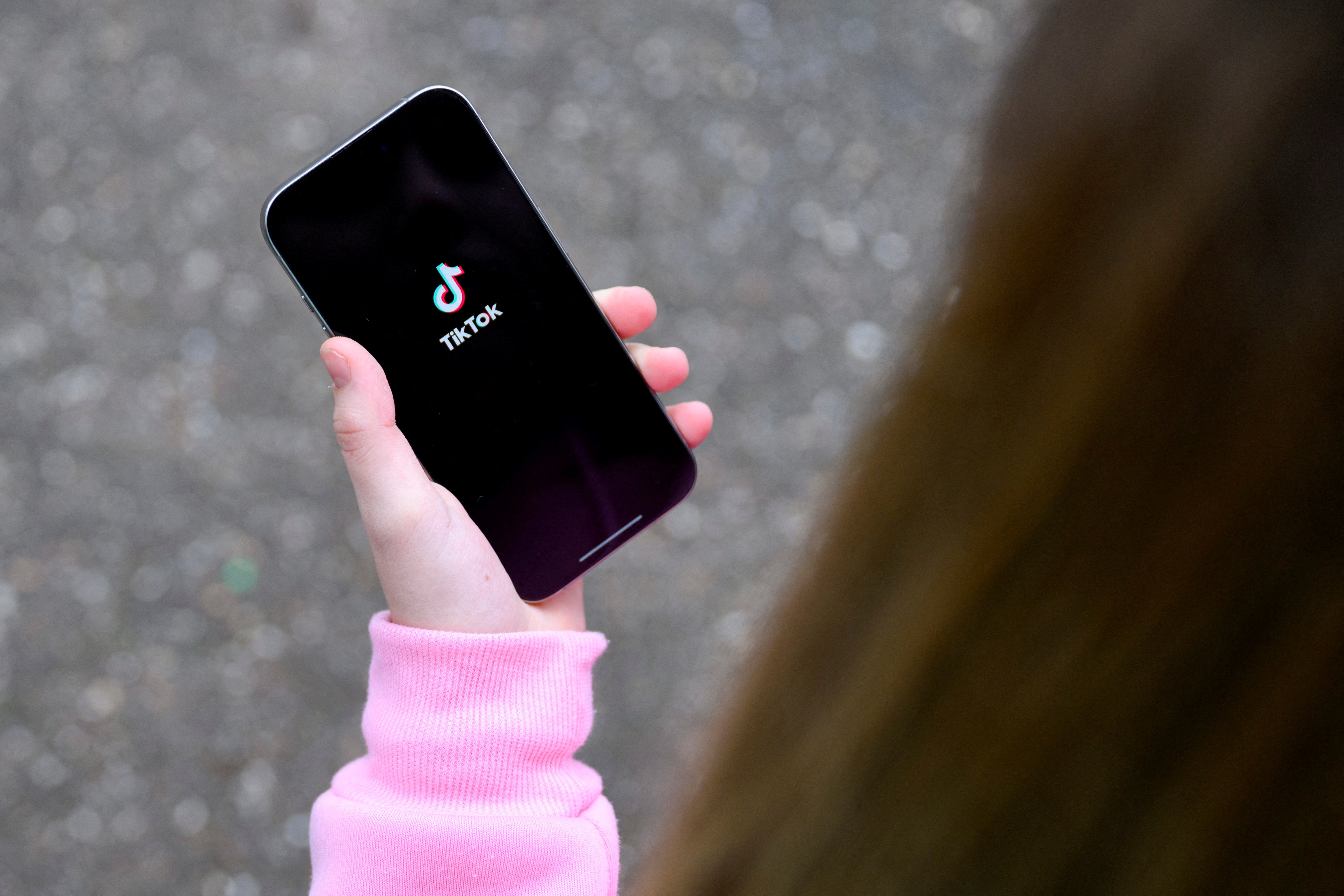 FILE PHOTO: A teenager poses for a picture with a phone displaying the TikTok logo, in Bonn, Germany, February 20, 2026. REUTERS/Jana Rodenbusch/File Photo