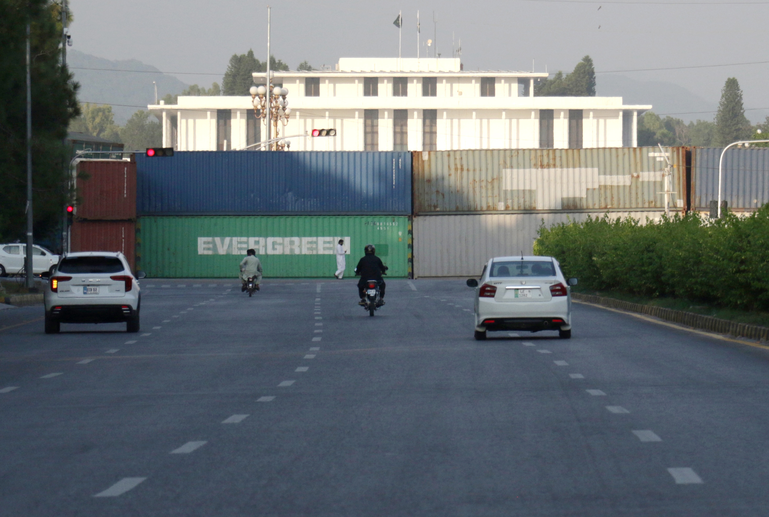 epa13248317 Commuters pass shipping containers lining Islamabads Red Zone, in Islamabad, Pakistan, 18 September 2026. Authorities have deployed containers and additional security personnel at key roads and entry points ahead of planned opposition protests and a Pakistan Tehreek-e-Insaf (PTI) long march scheduled for September 27, with the party demanding the release of former Prime Minister Khan. The security measures have disrupted traffic and raised concerns about restricted road access and the detention of commercial containers. EPA/SOHAIL SHAHZAD