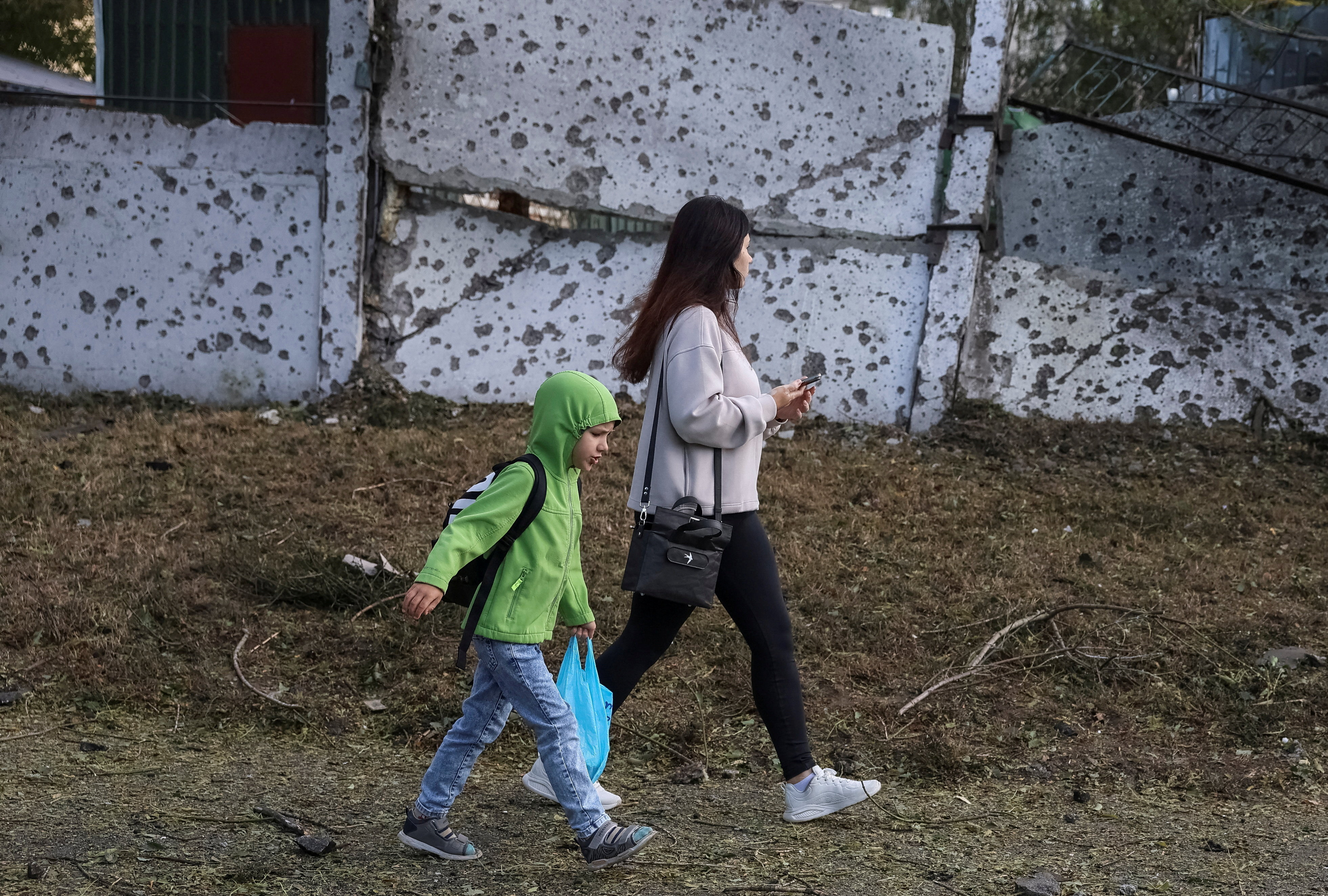 A woman and a boy walk near a fence with traces of shrapnel at a site of a Russian missile strike, amid Russia's attack on Ukraine, in Kyiv, Ukraine September 8, 2026. REUTERS/Stringer TPX IMAGES OF THE DAY
