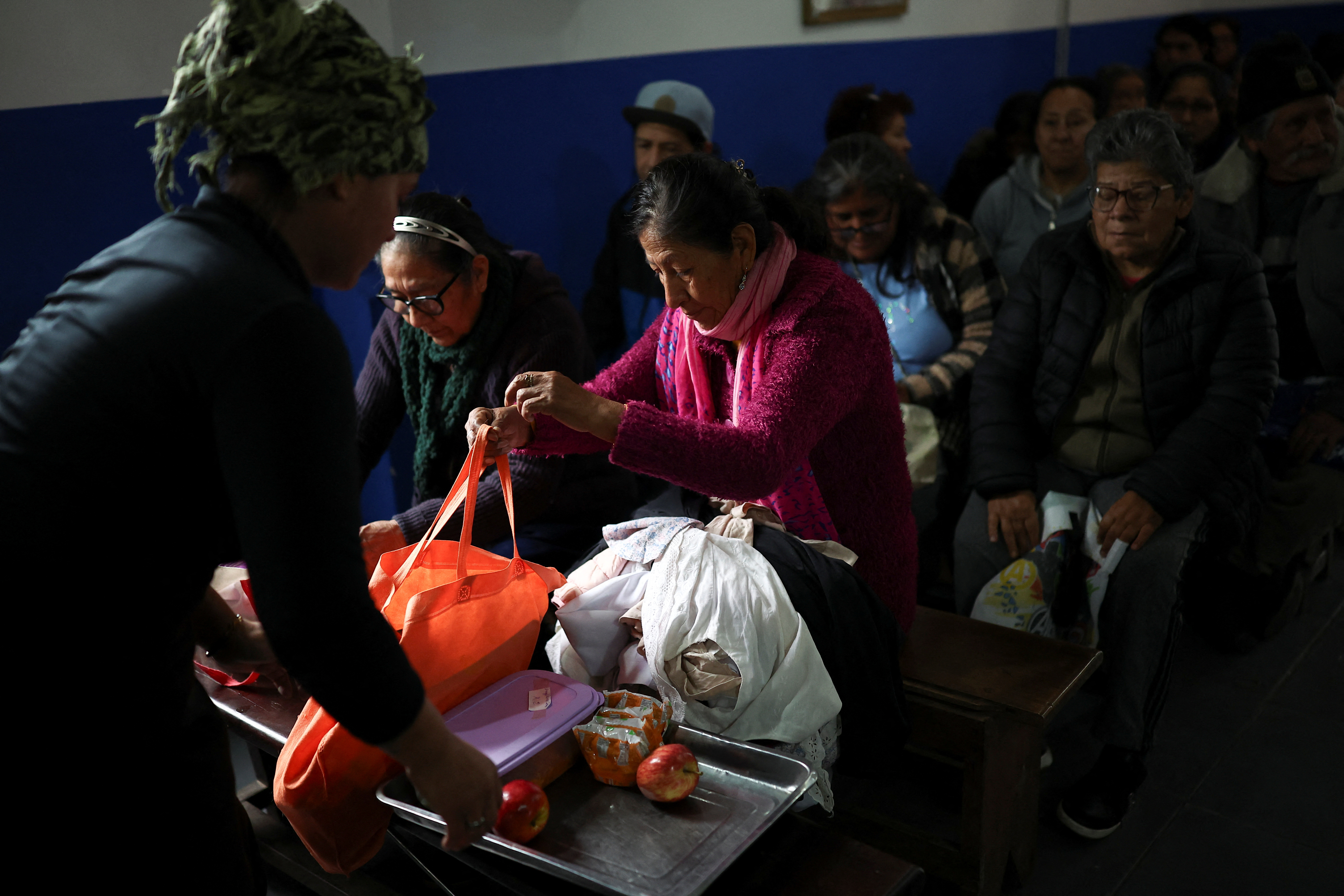 People sit inside a chapel while waiting for a meal distribution, as soup kitchens, barter clubs and families taking out short-term loans for groceries are exposing the social strains emerging under Argentine President Javier Milei's austerity program, barely a year before Argentina's next presidential election, in Buenos Aires' Villa 31 neighborhood, Argentina, August 28, 2026 [Agustin Marcarian/Reuters]