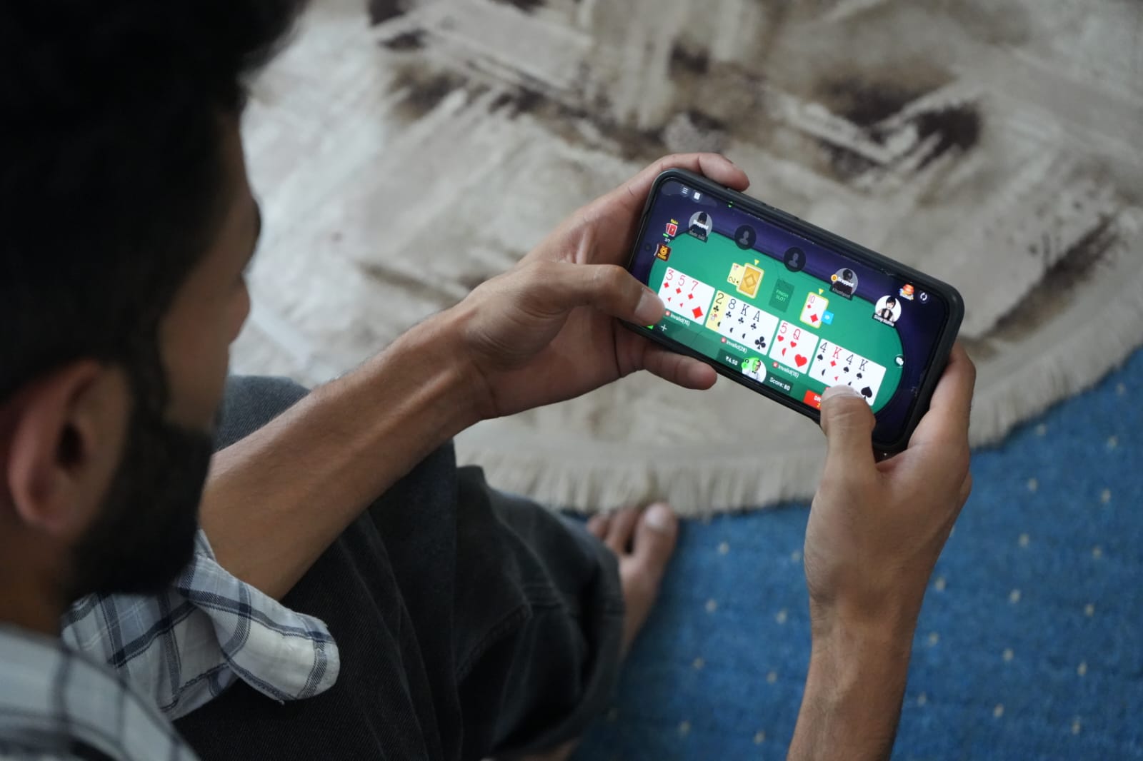 A young Indian man playing a money-based card game on his phone