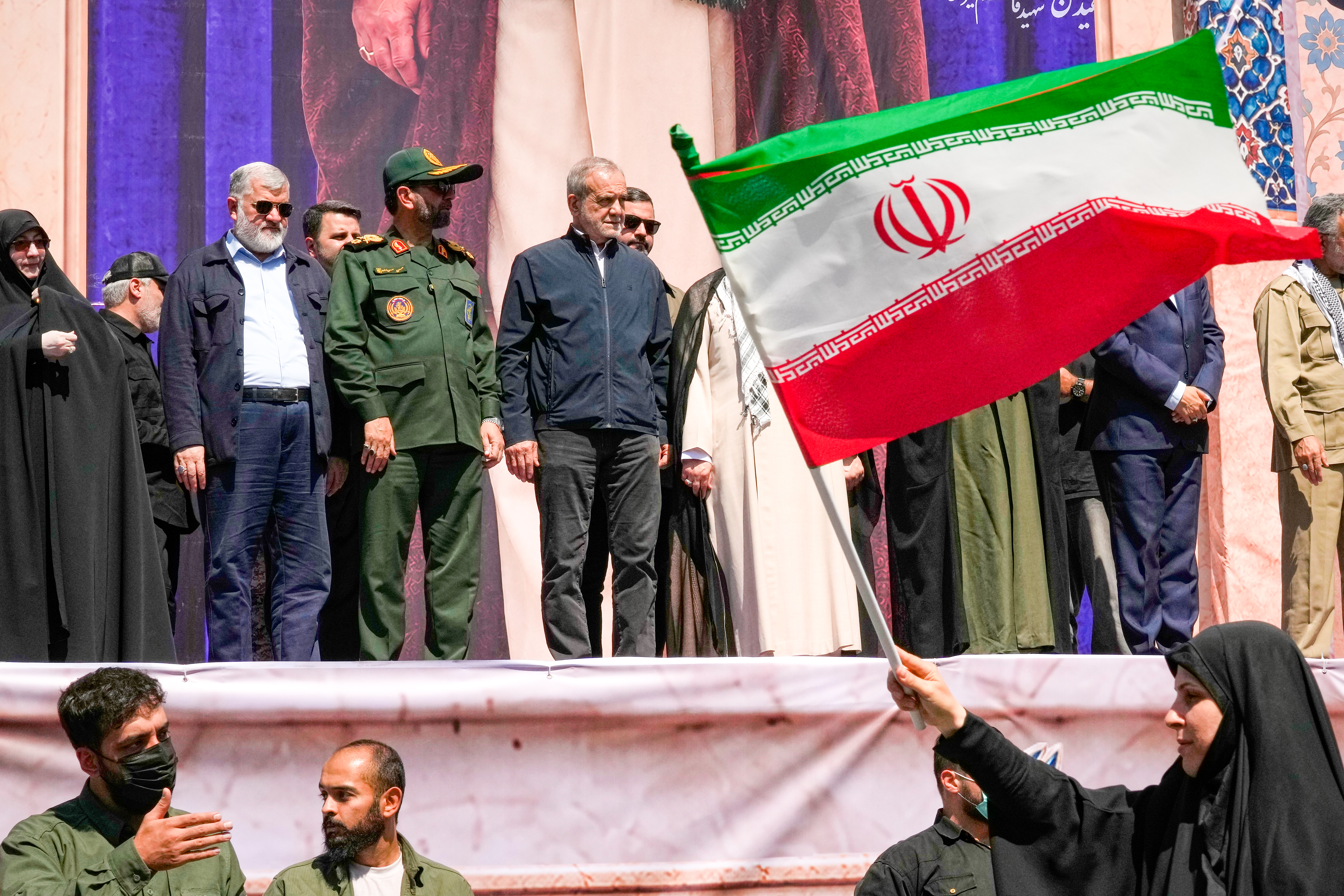 Iranian President Masoud Pezeshkian, center left, and other officials watch as a woman waves an Iranian flag during the state-organized "Janfada," or "Sacrifice for Iran," military-style parade in Tehran, Iran, Friday, Sept. 18, 2026. (AP Photo/Vahid Salemi)