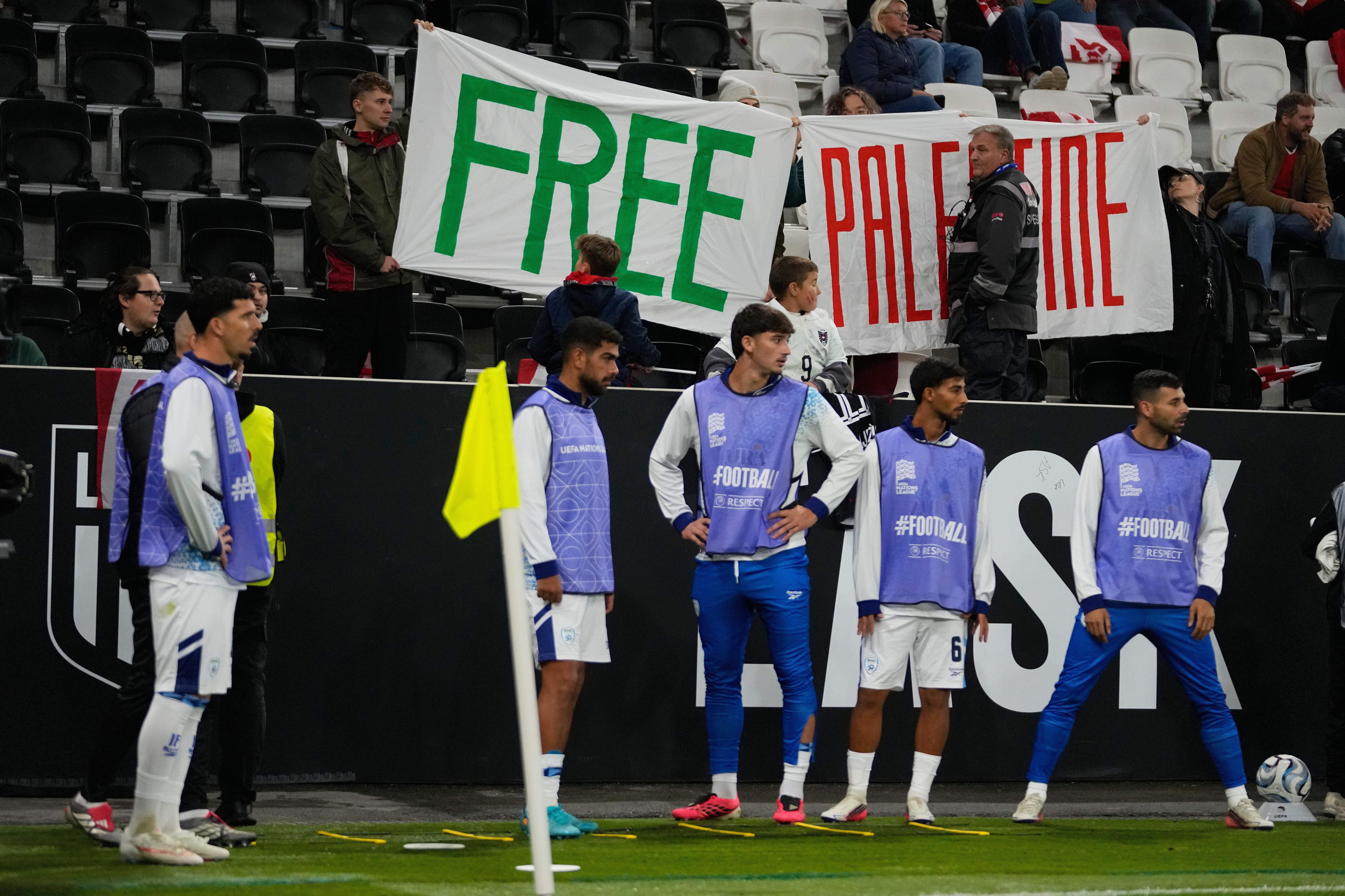 Players of Israel warm up as protesters hold up banners.