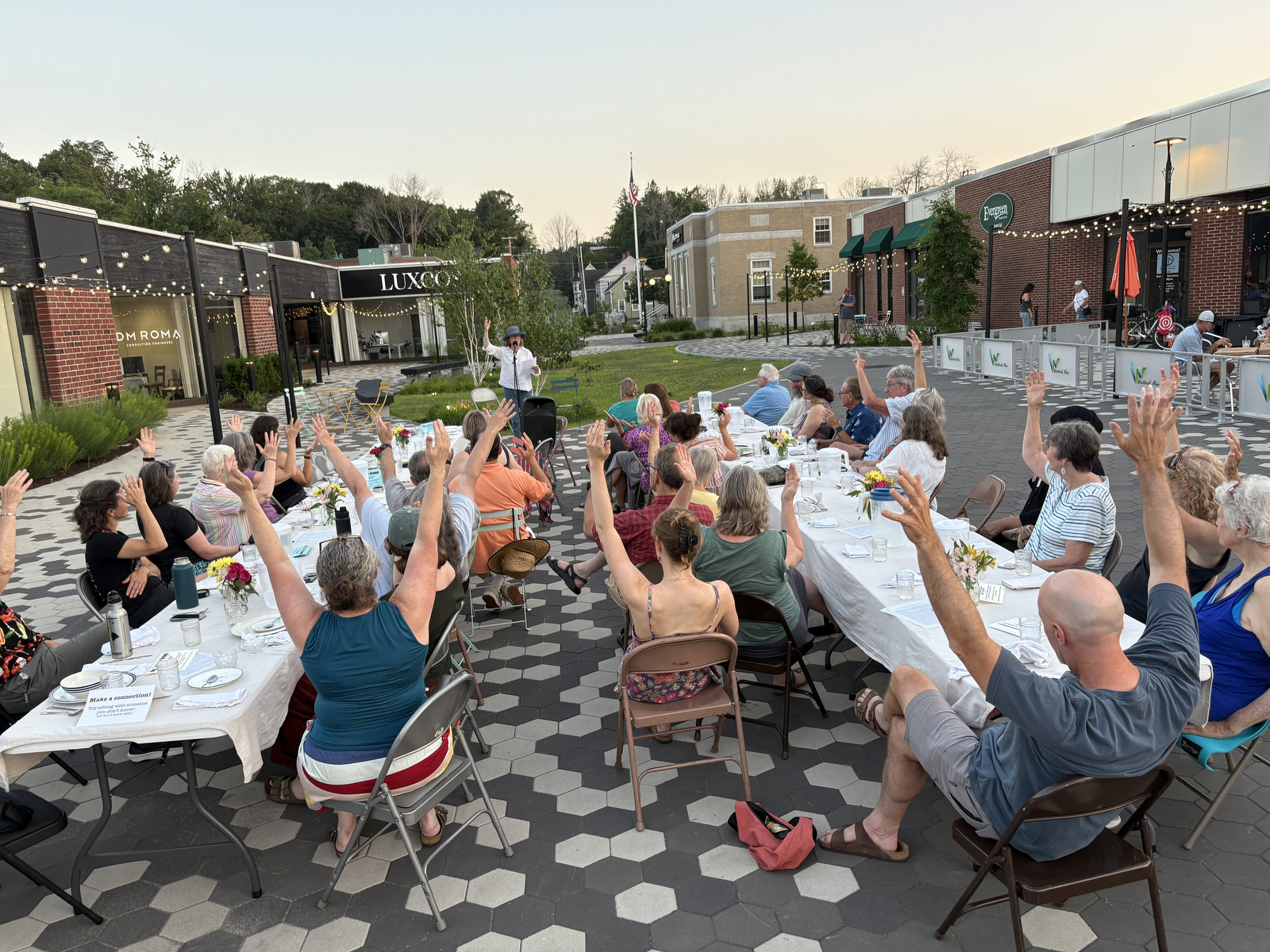 Community members raise their arms during a gratitude poem at a supper in Westbrook, Maine, in July 2025 [Courtesy of Community Plate]