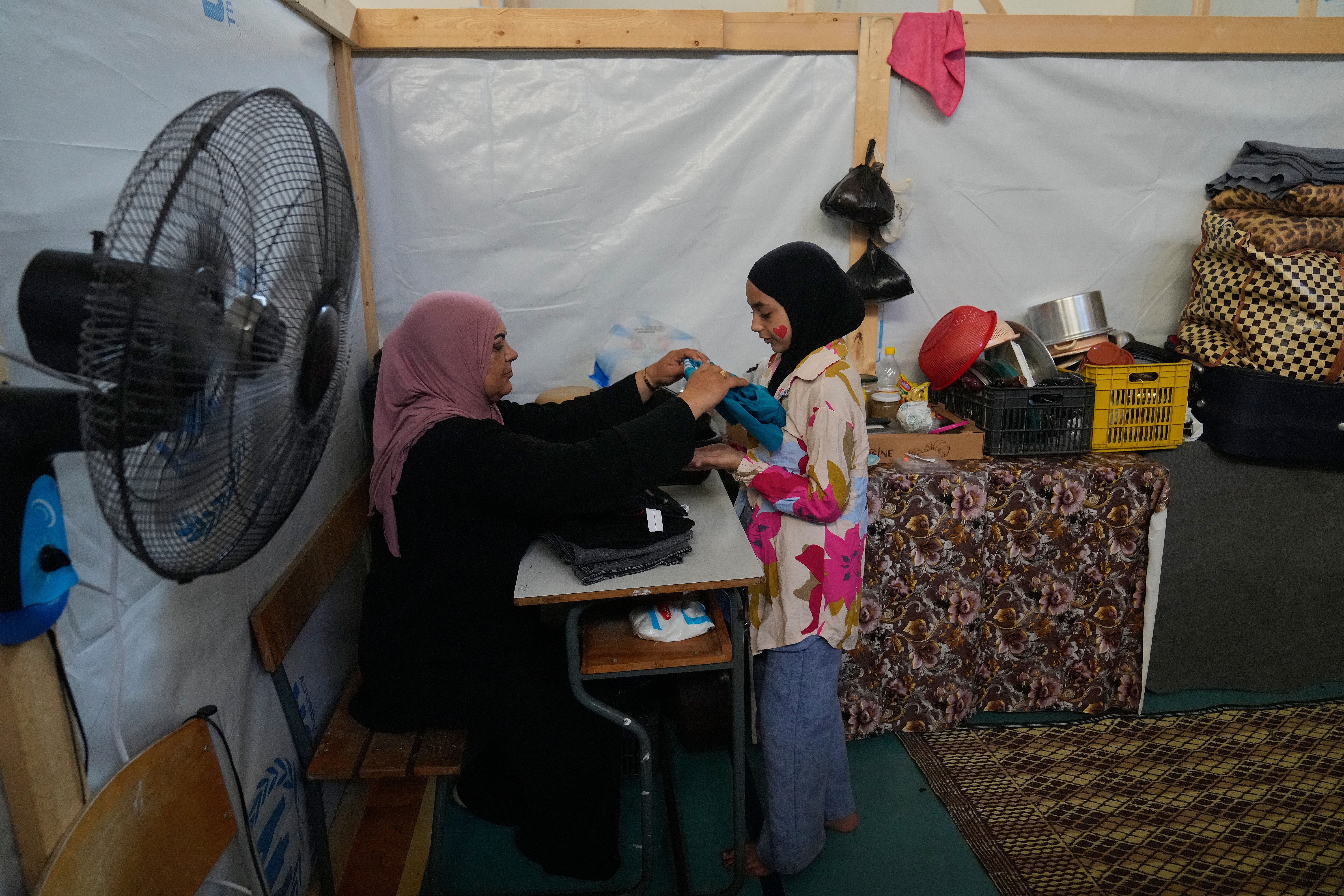 Displaced Randa al-Taki, 51, and her daughter Fatima Khashab, 11, arrange their clothes inside a makeshift room that was set on a basketball court inside a public school turned into a shelter for people whose villages in southern Lebanon were destroyed or occupied by Israeli forces, in Tyre, southern Lebanon, Thursday, Aug. 27, 2026. (AP Photo/Hussein Malla) CORRECTION: Last name corrected to Khashab, instead of Haidar