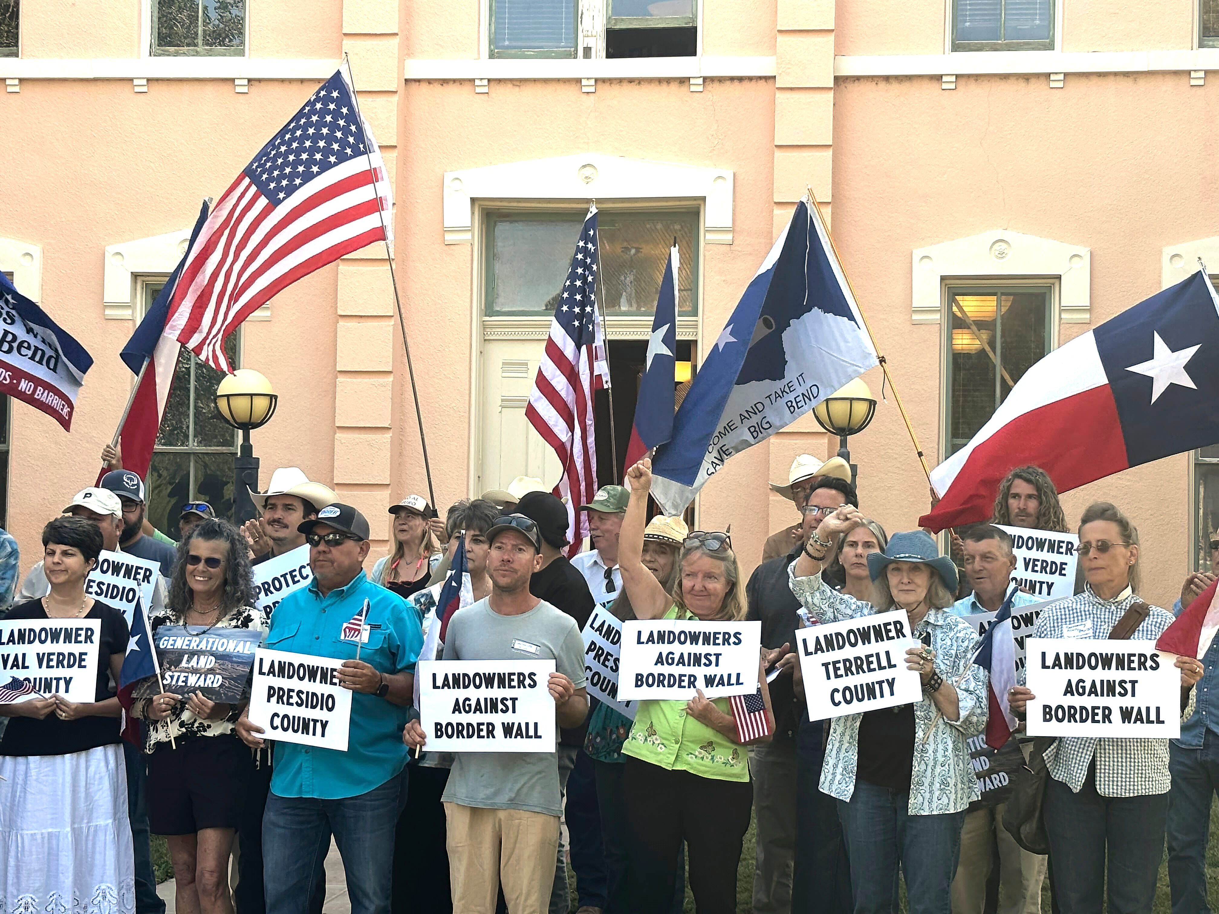 People stand at the roadside holding handmade protest signs.