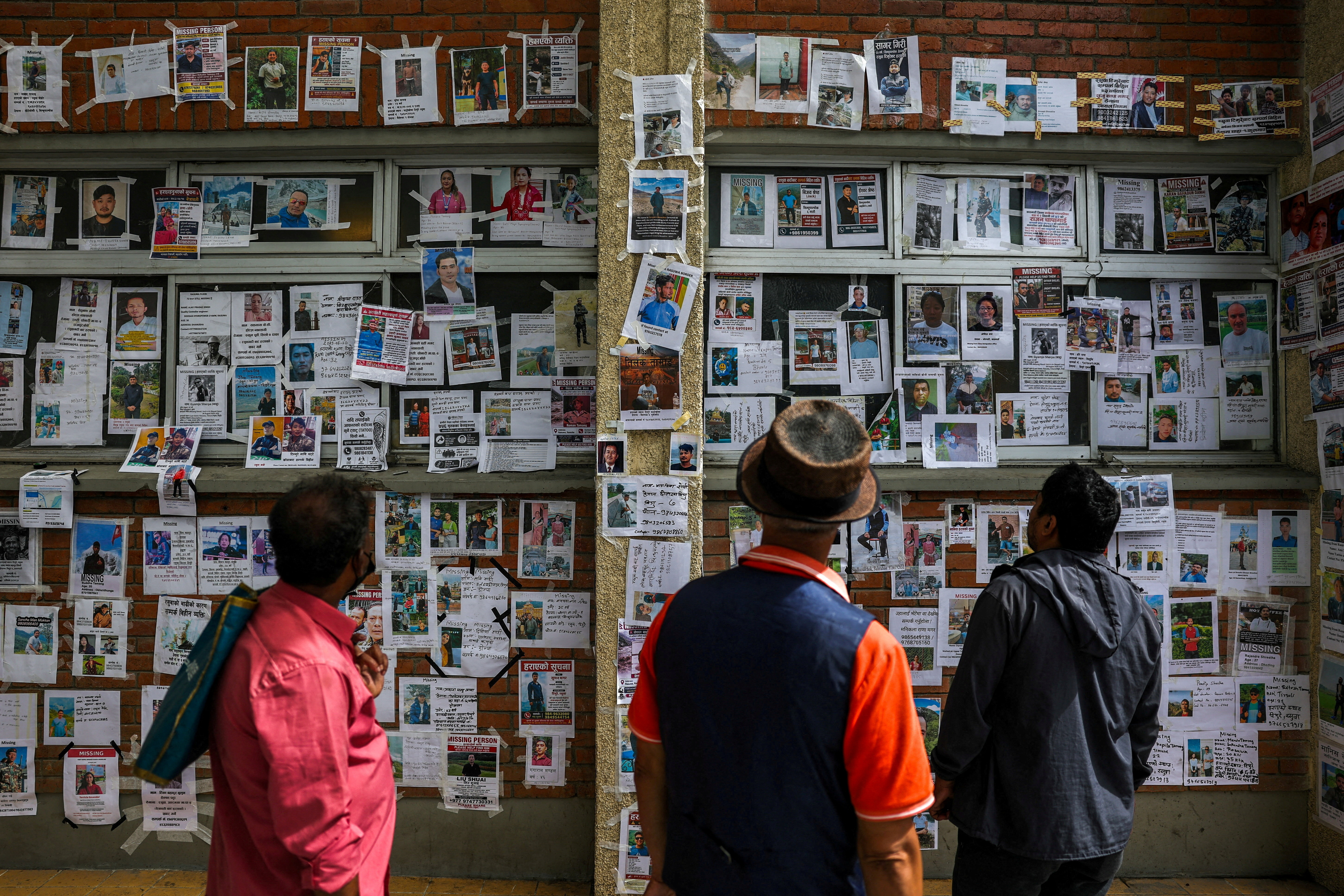 People look at photographs of missing people on a wall.